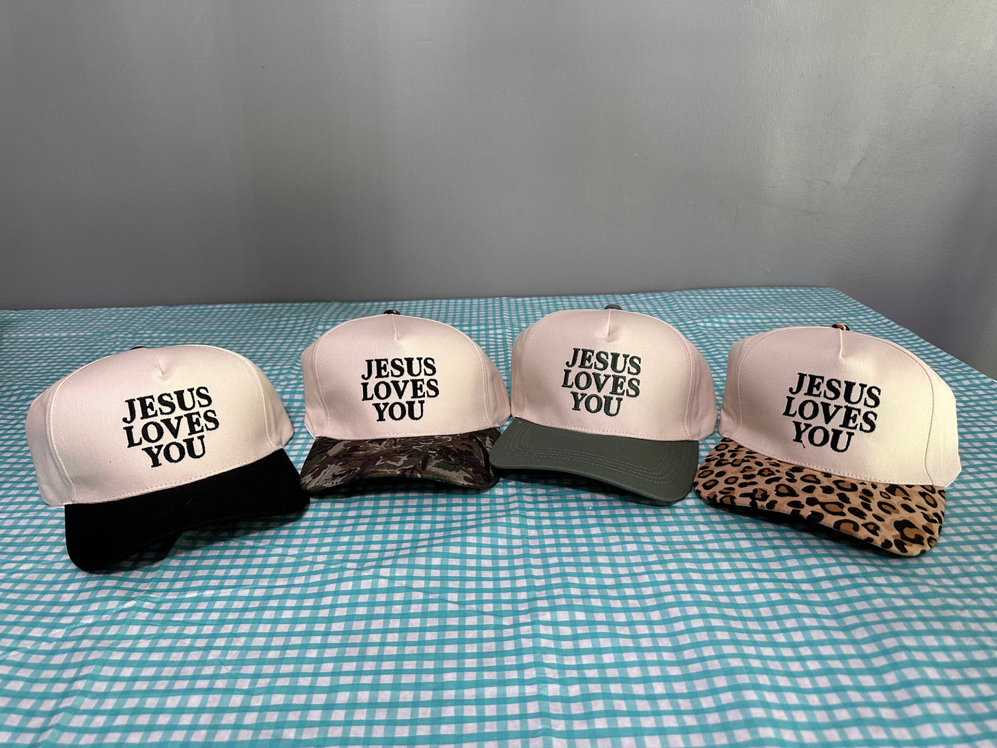 Four caps with 'Jesus Loves You' text on a checkered tablecloth.