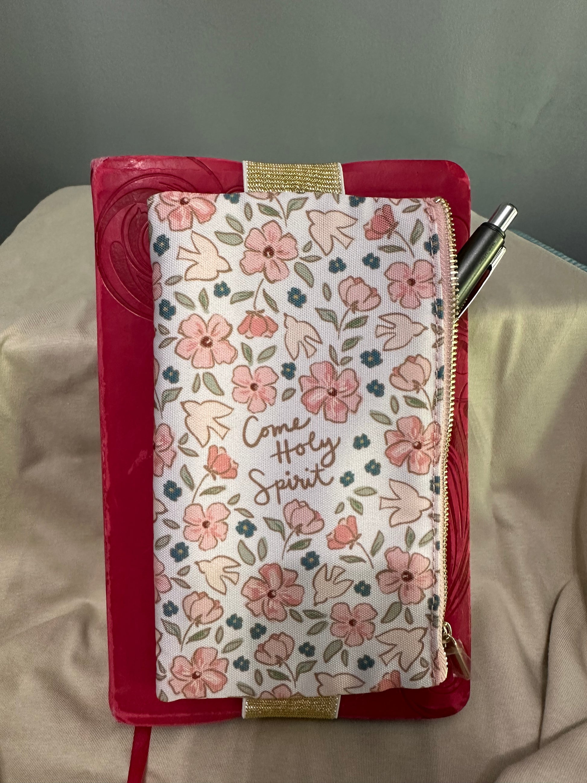 Floral pouch with 'Happy Spring' text on a red border, held by a pen.