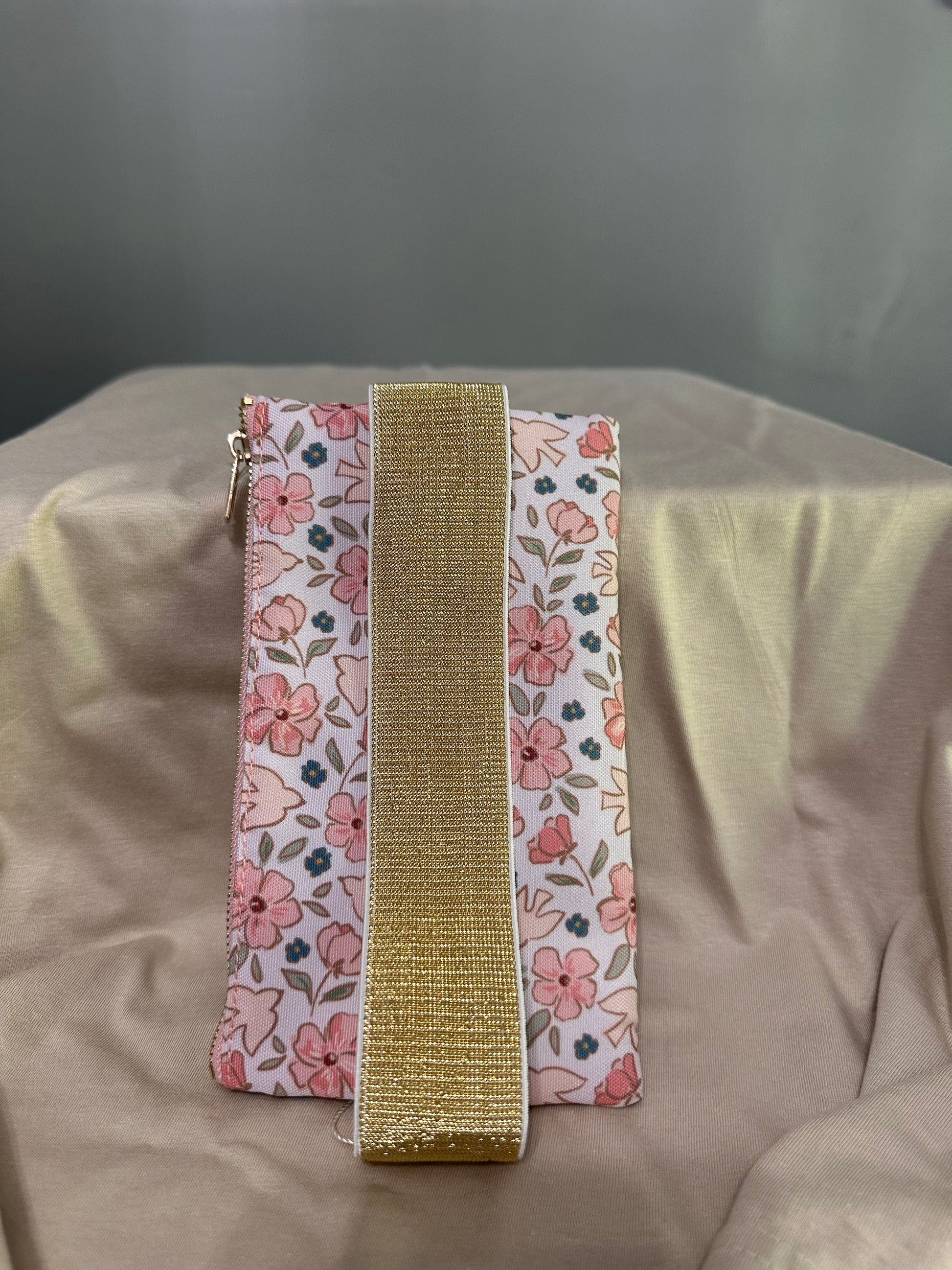 Two floral-patterned ribbons with a gold band on a beige fabric background