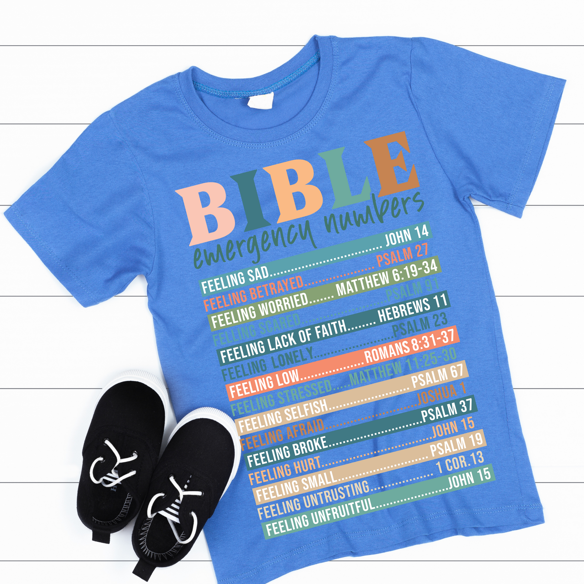 A person wearing a white long-sleeved T-shirt with 'BIBLE emergency numbers' printed in colorful letters, followed by lists of Bible verses.